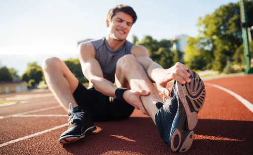 Ein Sportler sitzt auf einer Tartanbahn und dehnt seinen Fuss